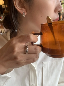 Détail d'une bague matelassée argentée et de créoles torsadées portées par un mannequin