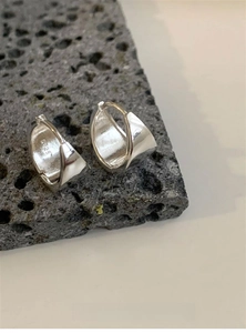 Detail of S925 sterling silver triangular earrings on a dark volcanic rock surface
