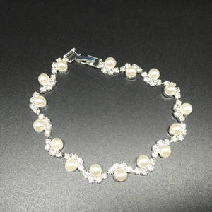 Dettaglio del bracciale ondulato argento con perle e strass su uno sfondo nero granuloso