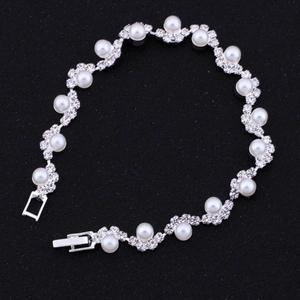 Dettaglio di un bracciale da sposa argento con strass floreali e perle bianche su sfondo nero