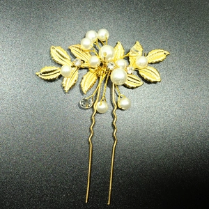 Détail d'une épingle à cheveux de mariée dorée avec perles et feuilles d'olivier sur fond noir
