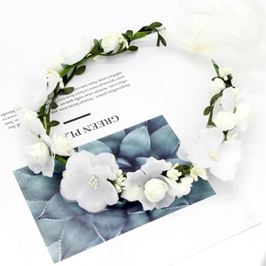 Detail of white floral wreath featuring textile roses, green leaves and adjustable ribbons