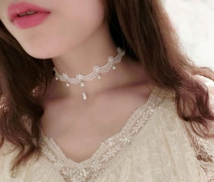 Dettaglio ravvicinato del choker in pizzo bianco con eleganti ciondoli di perle al collo