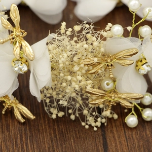 Gros plan sur un bijou de tête avec libellule dorée, fleurs blanches et perles nacrées
