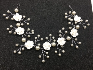 Close-up of white handmade clay roses and faux pearls on silver bridal hair vine