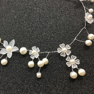 Close-up of white handmade matte resin flowers and pearls on bridal hair vine
