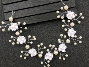 Macro detail of bridal hair vine featuring white resin roses and faux pearls on silver wire
