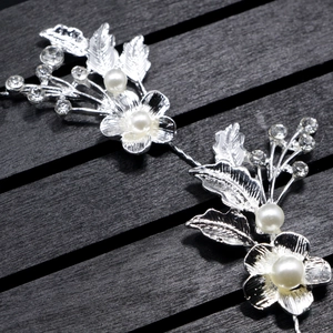 Detail of silver bridal hairpiece with rhinestone flowers and white pearls on wood