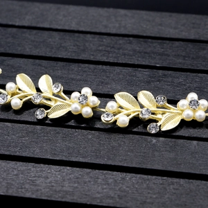 Close-up of golden bridal hairpiece with pearl beads, rhinestone flowers and leaf detail