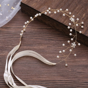 Dettaglio fascia da sposa con perle, cristalli e nastro bianco su sfondo di legno
