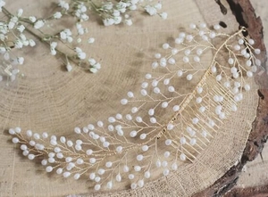 Detailed view of handmade bridal hair comb with gold leaves and white pearls on wood