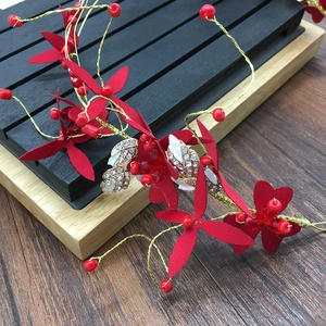 Vue détaillée des fleurs rouges et des perles dorées sur un serre-tête de mariée