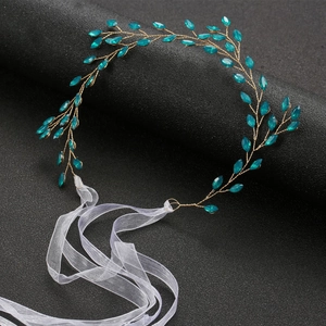 Detail of bridal hairband with emerald crystal leaves and golden wire on a black stand