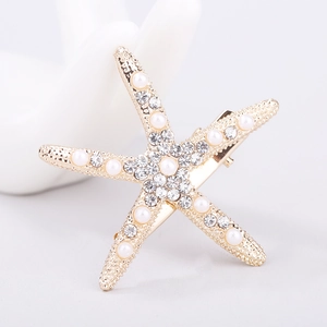 Close-up of golden starfish hair clip with white pearls and sparkling rhinestones
