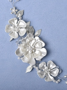 Gros plan d'un bandeau de mariée avec fleurs blanches, feuilles argentées et perles