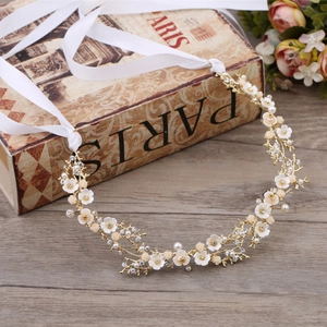 Détail d'un accessoire de mariée avec branches dorées, fleurs blanches, perles et cristaux