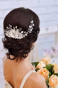 Détail de l'accessoire de mariée avec fleurs en tissu blanc et feuilles perlées sur les cheveux