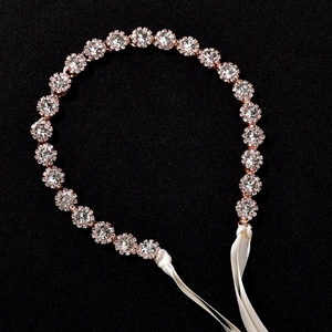 Détail d'un bandeau de mariée or rose avec fleurs en cristal et rubans de satin blanc