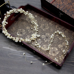 Detalle de diadema de novia artesanal con perlas y hilo dorado en bandeja de madera