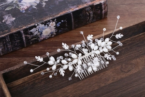 Elegant silver bridal hair comb with pearls, crystals, and hollow leaves on wood tray