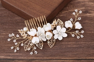 Détail de fleurs en tissu blanc avec feuilles dorées et perles sur un peigne de mariage