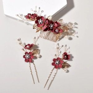 Close-up of bridal hair pins set with burgundy fabric flowers and golden metal leaves