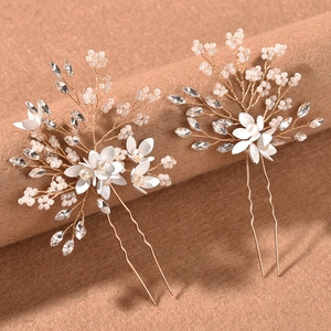 Pair of gold bridal hair pins with white enamel flowers and pearls on velvet stand