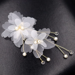 Détail d'une pince à cheveux fleur en tulle blanc avec perles et fils dorés sur noir