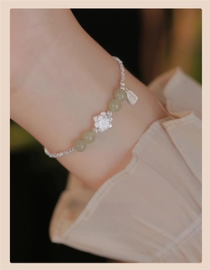Detail of S925 silver lotus pendant bracelet with green jade beads on woman's wrist