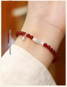 Detalle de pulsera de ágata roja natural con un colgante de pez koi de plata en la muñeca
