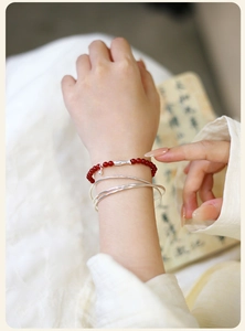 Detalle de pulsera de ágata roja con colgante de pez de plata y brazaletes finos a juego