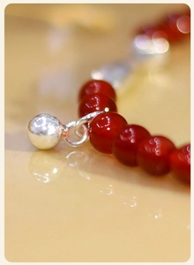 Detalle macro de cuentas de ágata roja y colgante de koi en plata en la pulsera