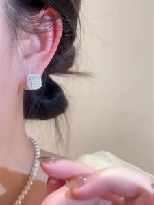 Close-up of square silver hoop earrings with pave diamonds on a model wearing pearls