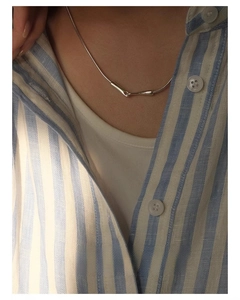 Close-up of geometric snake bone chain necklace with silver cylinders on striped shirt