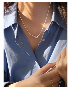 Detail of geometric silver tube pendant on snake chain worn over a light blue shirt