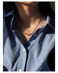 Close-up of minimalist silver knot pendant with sleek snake chain on a shirt
