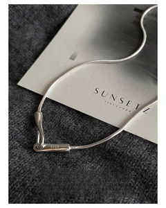 Macro shot of S925 sterling silver snake chain with cylindrical clasp on grey knit fabric