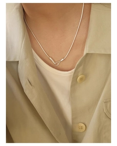 Close-up of minimalist silver snake chain necklace on a model wearing a beige shirt