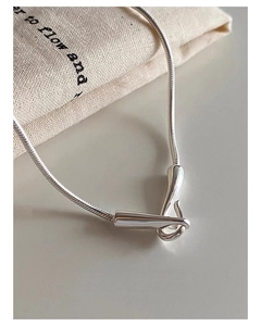 Close-up of minimalist silver snake chain with intertwined fluid metal pendant on linen