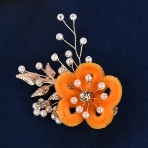 Vue détaillée d'une épingle à cheveux fleur orange avec perles et feuilles dorées