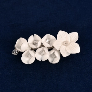 White handmade ceramic flower hair clip with crystals on a navy blue velvet background