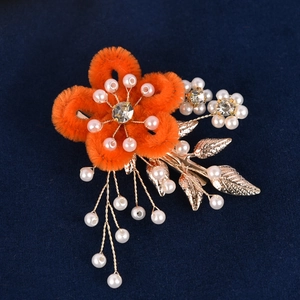 Détail d'une barrette fleur en peluche orange avec glands en perles et feuilles dorées