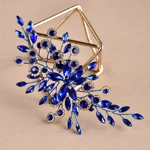 Close-up of golden leaf hair accessory with dark blue marquise crystals on warm sand background