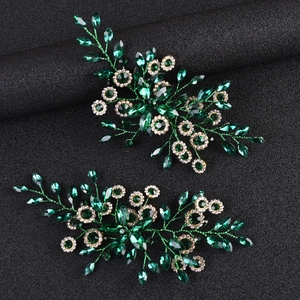 Detailed close-up of emerald green crystal leaf hair clips with gold wire and rhinestones