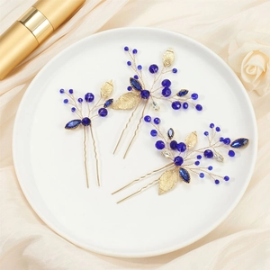 Detail of three handmade U-shaped hairpins with deep blue crystals and golden leaves
