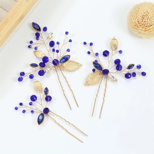 Detail of three handmade U-shaped hair pins with blue crystals and golden leaf accents
