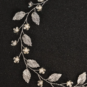 Detail eines handgefertigten Brautstirnbands mit Metallblättern und Perlenblüten