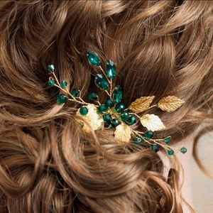 Elegant bridal hair comb with emerald green crystals and golden leaves on brown hair