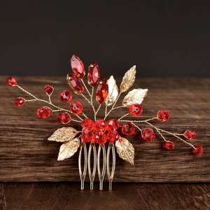 Close-up of red crystal beads and golden metal leaves on a handmade bridal hair comb