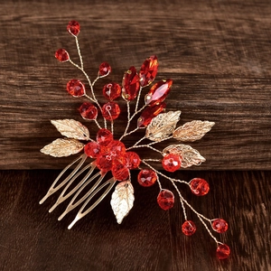 Close-up of golden leaf hair comb featuring vibrant red crystals on a vintage wood background